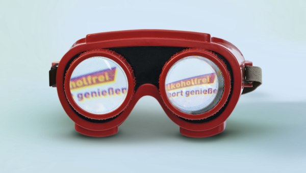 Ansicht auf eine rote Rauschbrille: Darin der Schriftzug „Alkoholfrei Sport genießen“