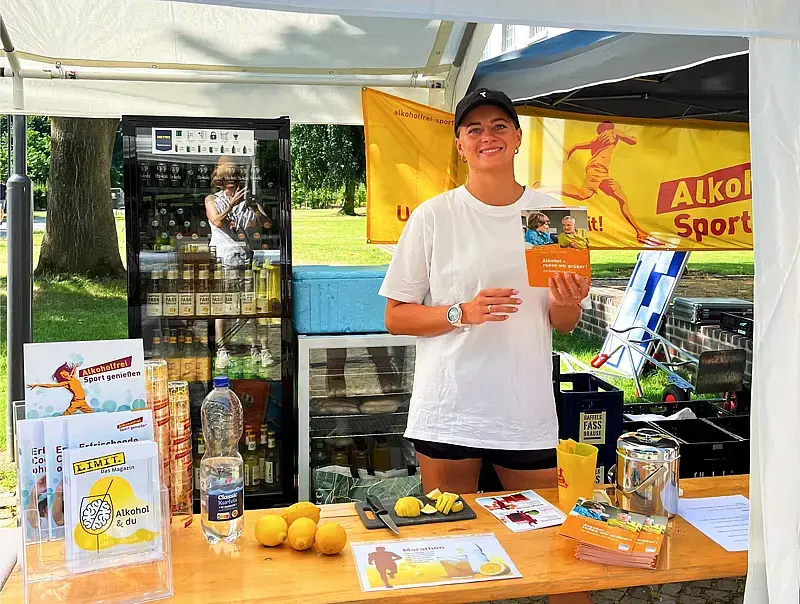 Junge Dame hinter dem einladend gestalteten  „Alkoholfrei Sport genießen“-Infostand.