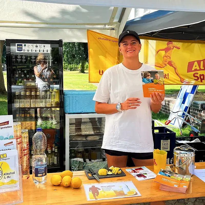 Junge Dame hinter dem einladend gestalteten  „Alkoholfrei Sport genießen“-Infostand.