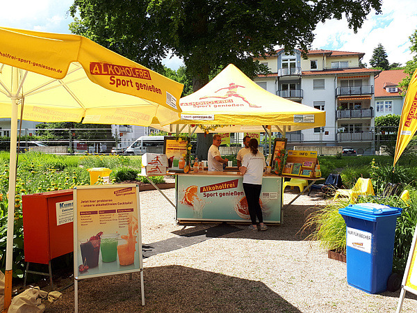 Ansicht eines Cocktailstandes und eines Sonnenschirms mit Aufschrift Alkoholfrei Sport genießen 