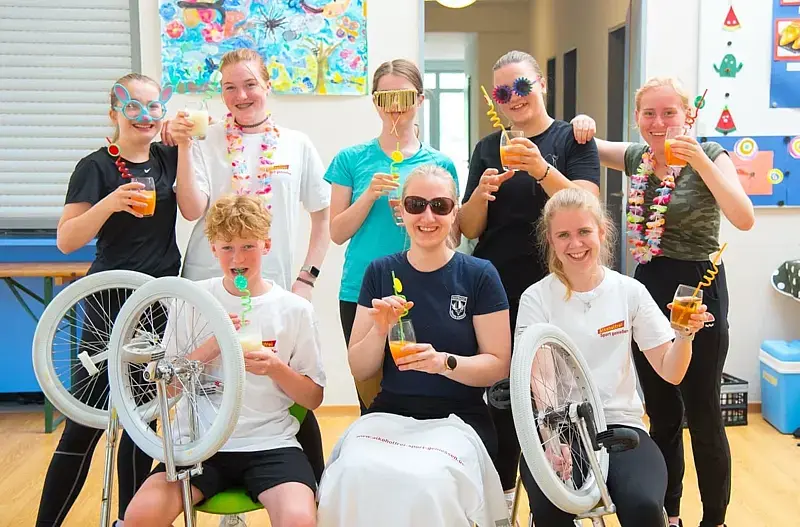 Jugendliche Einradfahrerinnen und -fahrer in Feierlaune: Sie halten leuchtend bunte Cocktails mit Ringelstrohhalmen in der Hand. 